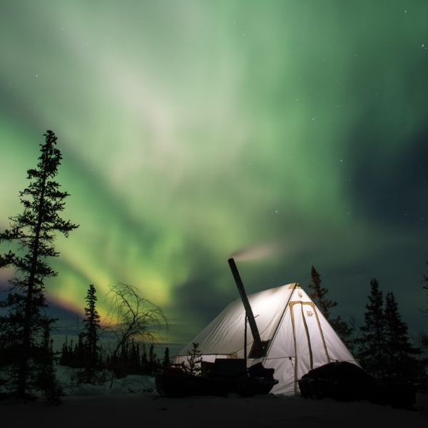 canvas tent with tent stove at night with northern lights