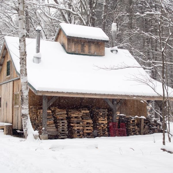 barn in snow with firewood pile under shed