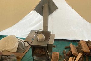 stove inside of tent with kettle and firewood