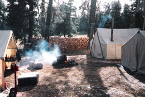 hunting camp with multiple canvas tents and campfire during the day